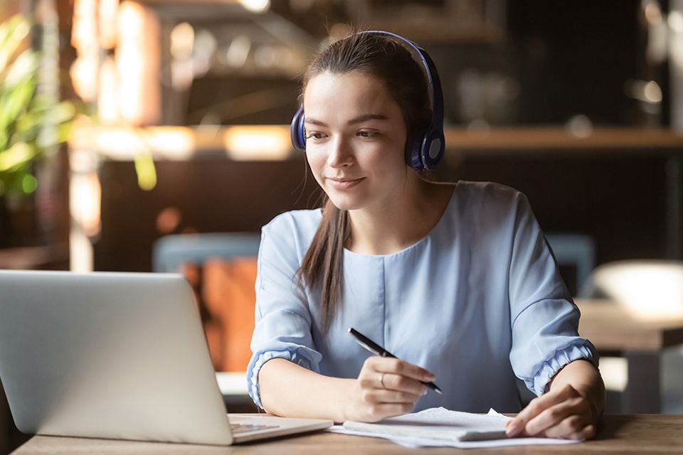 female college student sitting at desk with headphones on looking at laptop