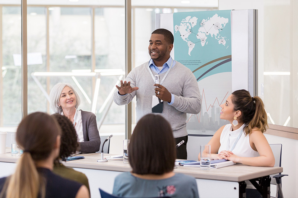 man in office building holding microphone and presenting to group of student