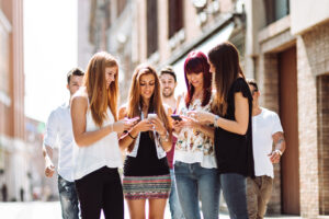 group of female college students looking at their smartphones with men approaching behind them