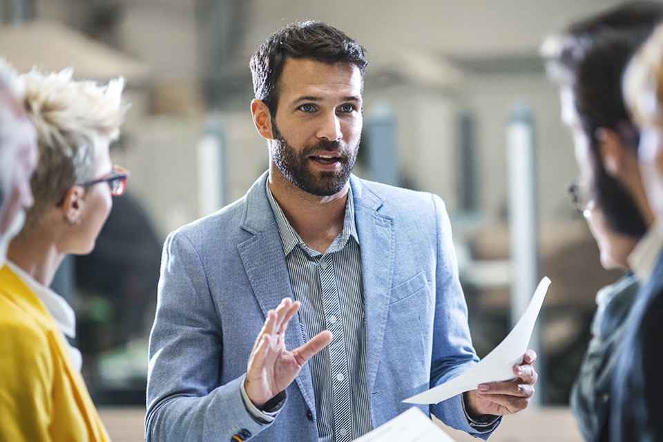 man holding paper document and speaking with colleagues