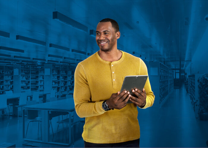 IT leader in yellow shirt holding tablet on background of classroom with blue overlay